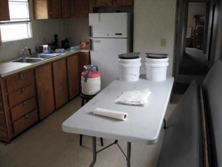 Table in a kitchen with two buckets and a roll of paper on top of it.